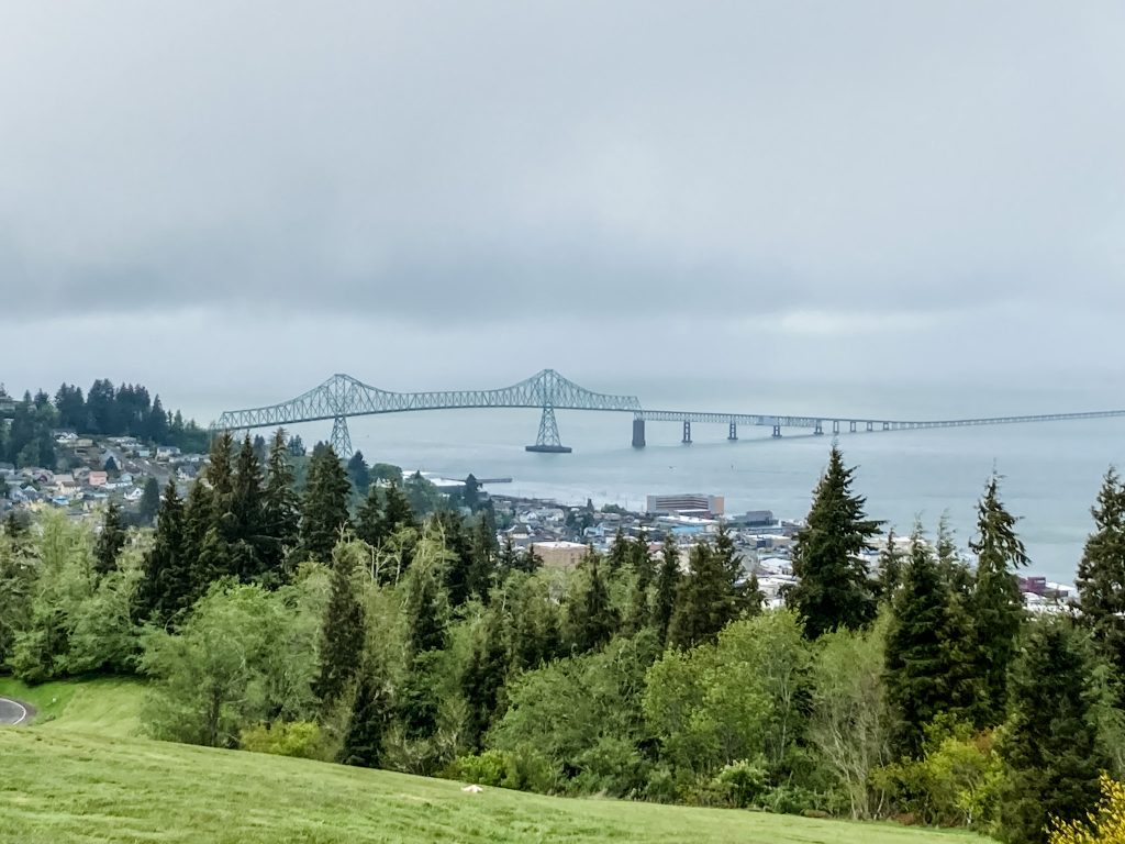 Green Astoria-Megler Bridge peeks over a cluster of green trees, linking Oregon and Washington.