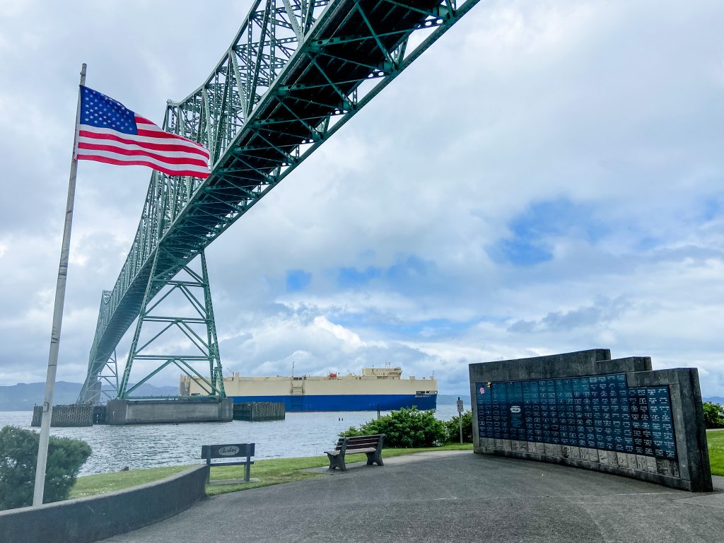 Maritime Memorial Park in Astoria, Oregon, with an American flag and Astoria-Megler Bridge in the background.