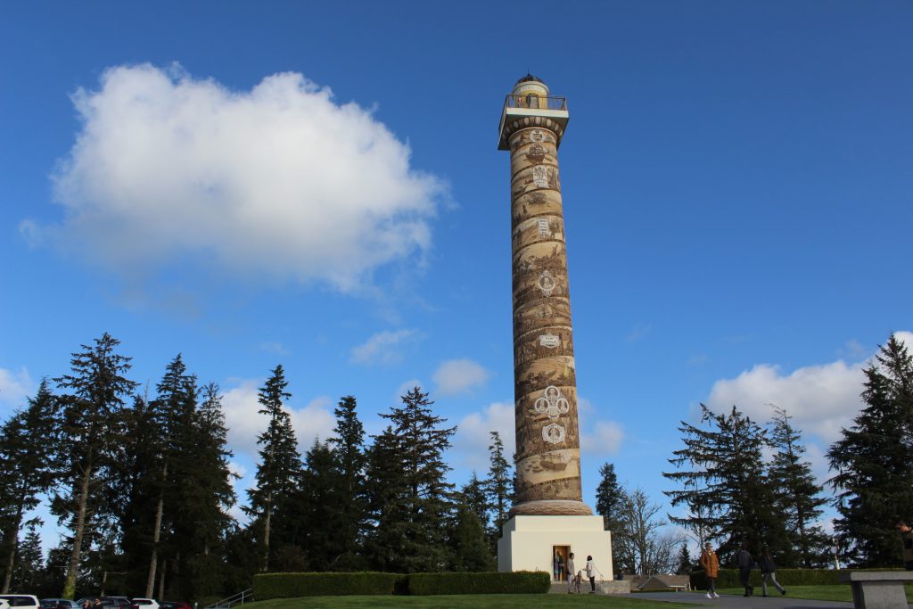 The Astoria Column stands tall against a background of pine trees and a deep blue sky.