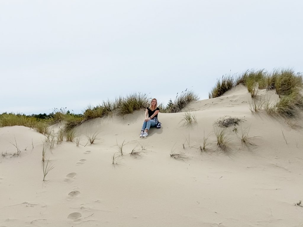 The author sits on a tall sand dune, surrounded by beach grass. A trail of footprints leads to the top of the dune.