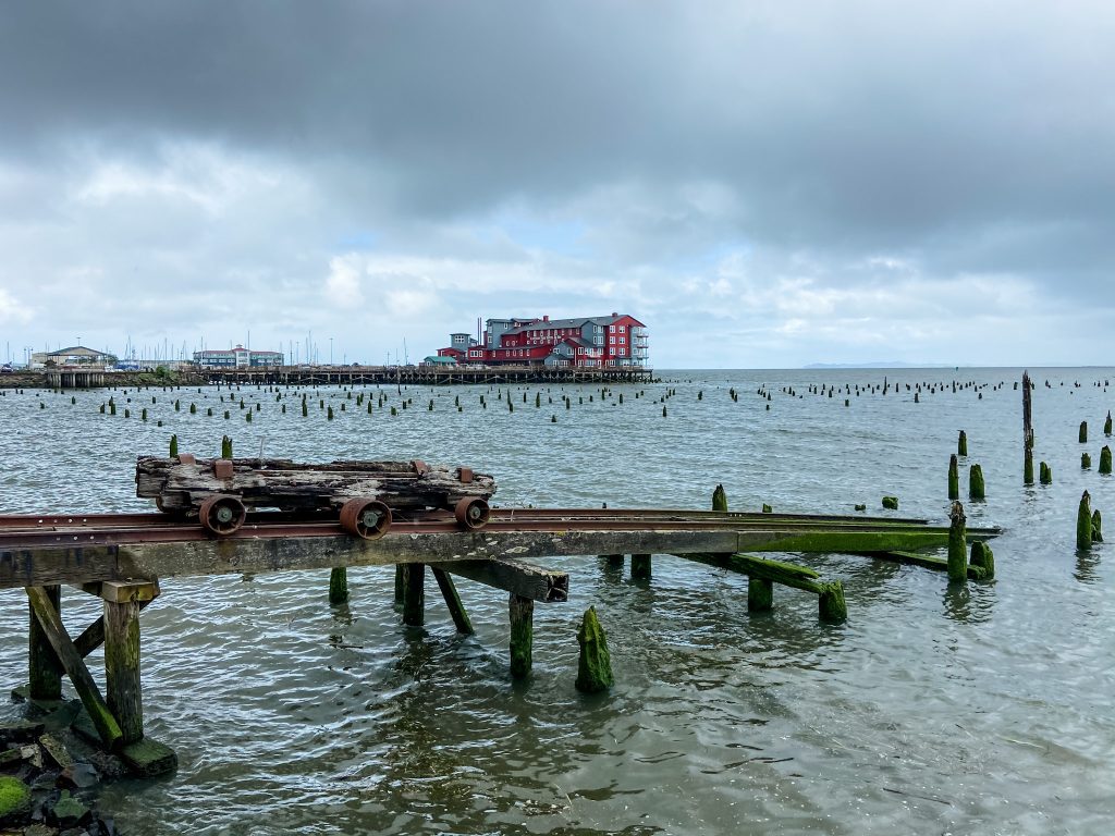 Pier with modern red building and pier with old, abandoned railroad equipment sit on the Columbia River.