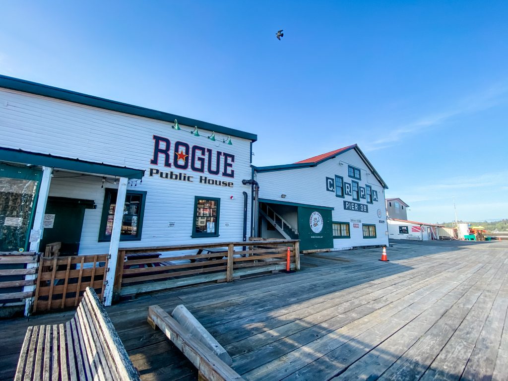 Rogue Public House, a brewery in Astoria Oregon, sits on a historic wooden pier against a blue sky background.