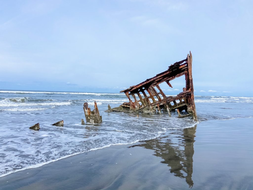Wreck of the Peter Iredale: the rusted remnants of the ship's bow sits in the sand, lapped at by waves.